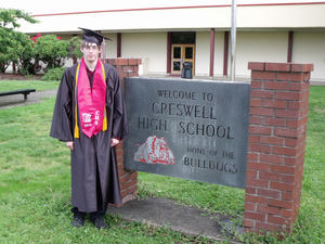 The author standing in front of his high school in black and red graduation gown, Creswell High School