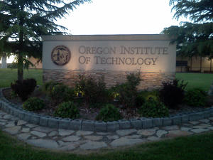 School sign for Oregon Institute of Technology underlit by lamps at dusk
