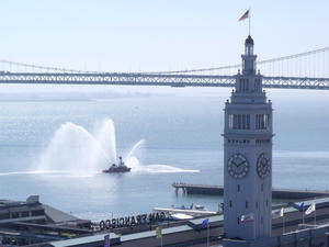 The ferry building in San Francisco, with a fire tugboat spraying water behind it as seen from the author's second year apartment during his Amazon Music internship